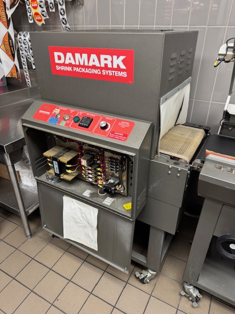Commercial DAMARK shrink packaging equipment being serviced in a kitchen